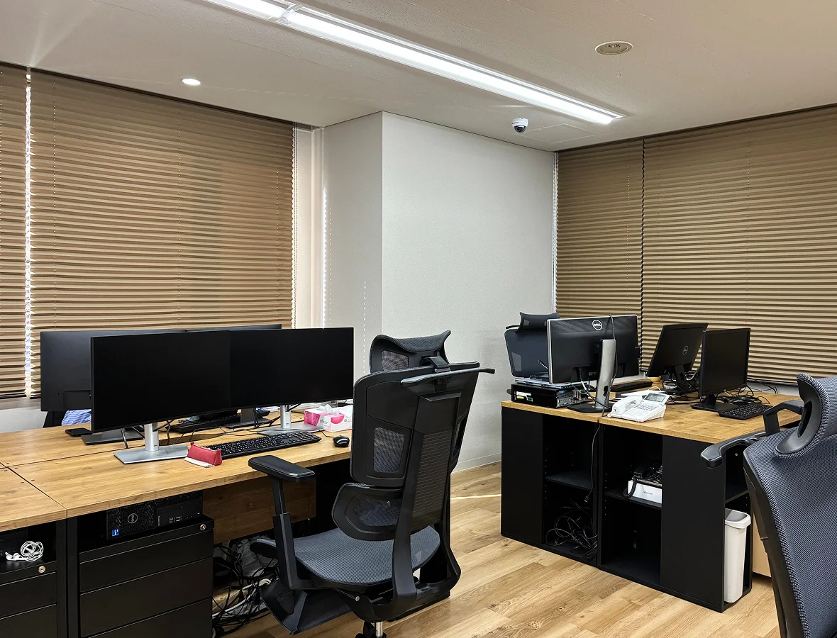 オフィス環境の写真。木製の机とヘッドレスト付きの椅子があり、机上には23インチのモニターが置かれている。