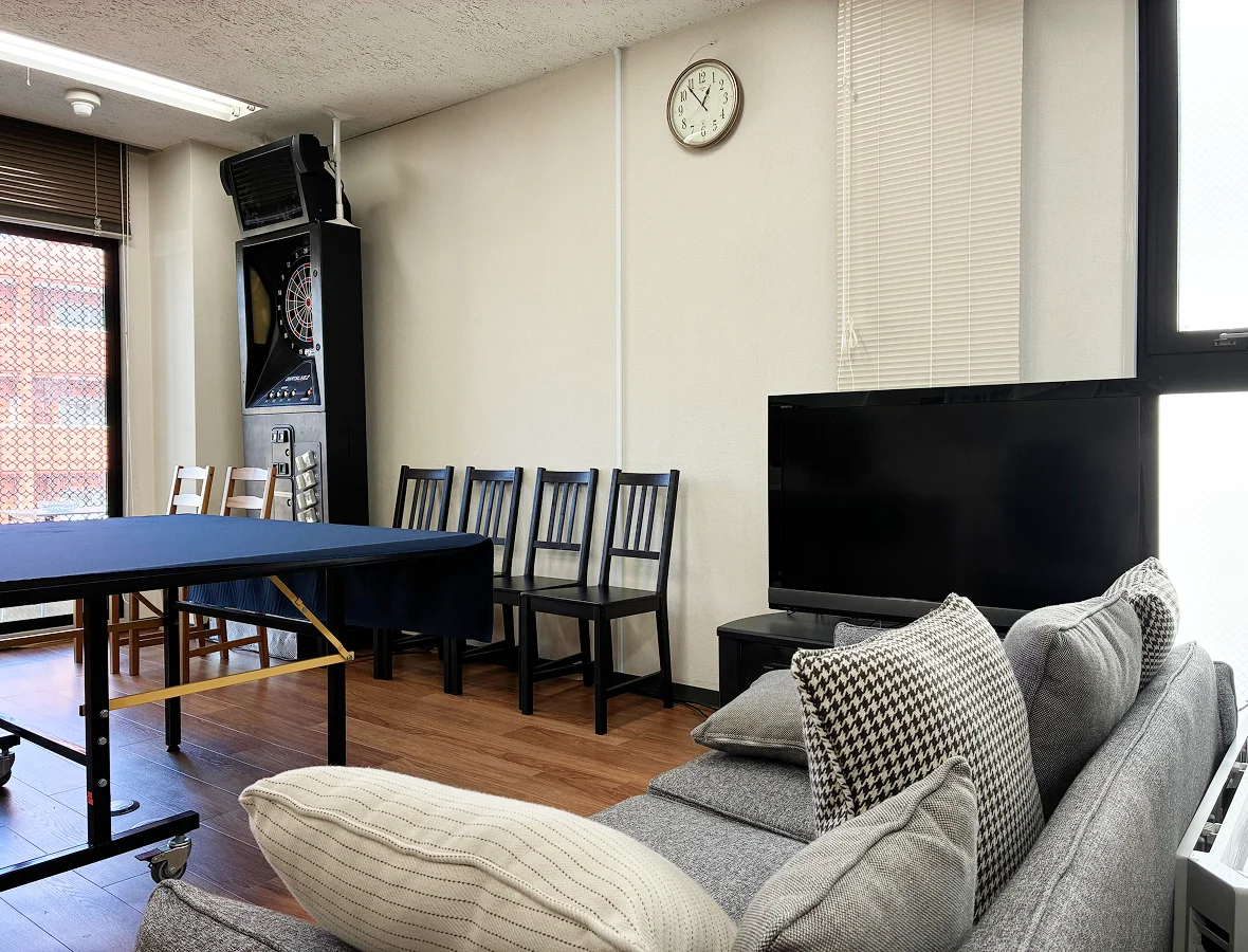 フリースペースの写真。手前にクッションとソファー、その横にテレビが置いてあり、奥には卓球台とダーツが設置されている。